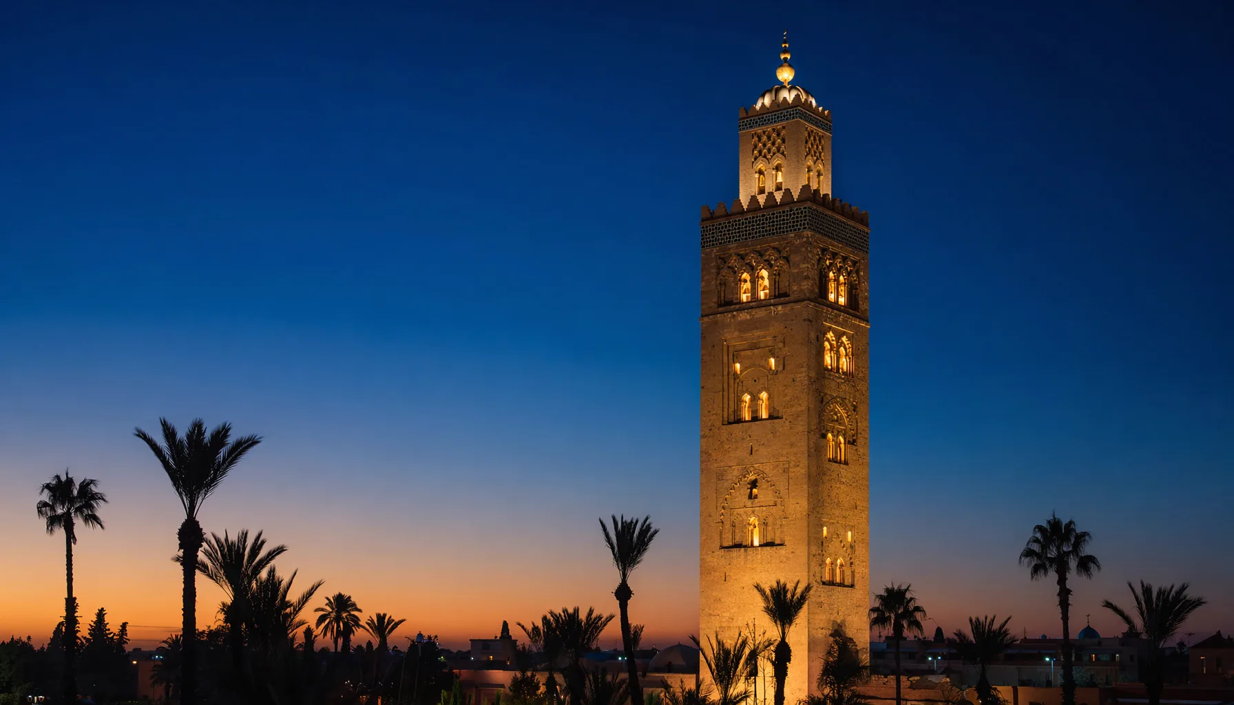 Minaret de la Koutoubia de Marrakech à l'aube, ciel bleu profond, lumières de la mosquée allumées