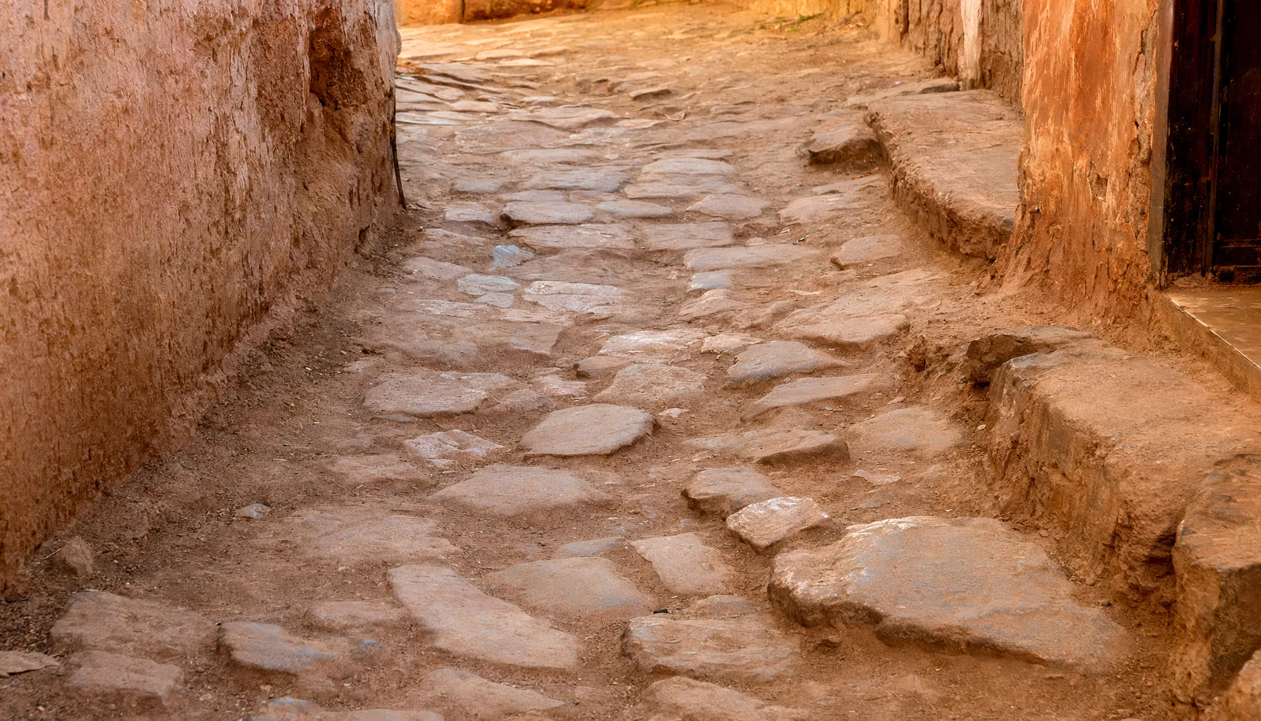 Ruelle pavée irrégulière de la médina de Marrakech, pierres et sol en terre, conditions typiques de marche