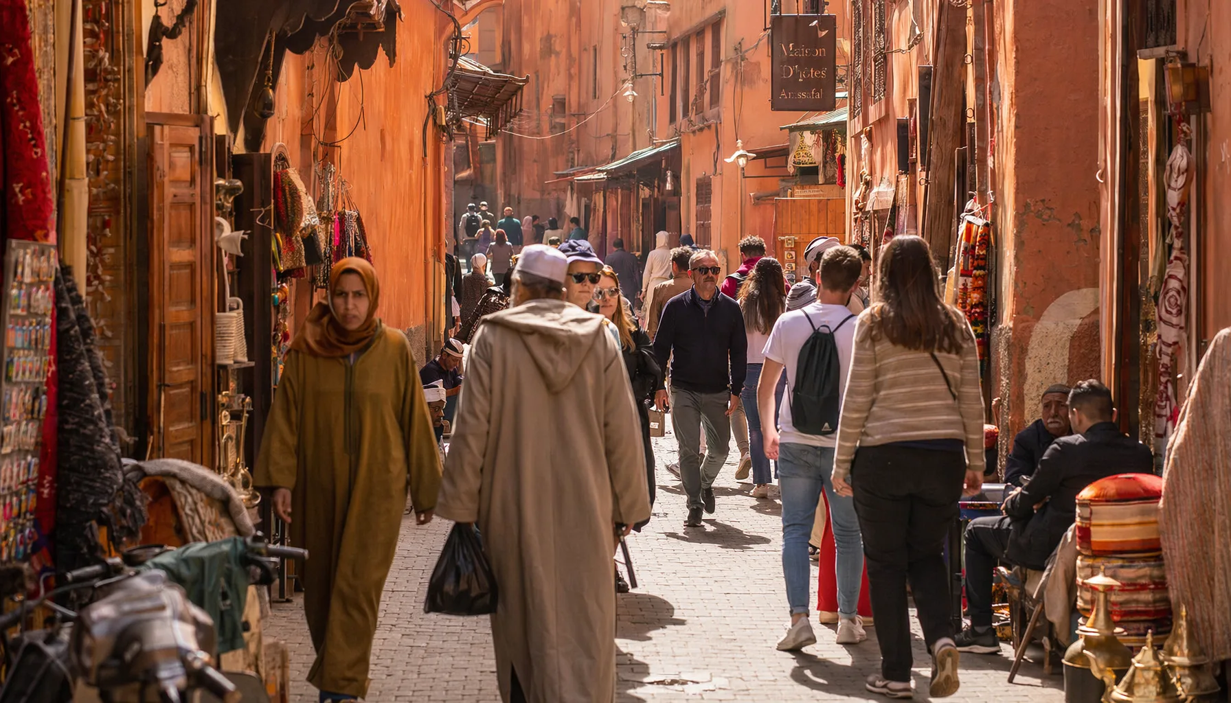 Rue animée de la médina de Marrakech en journée, touristes et habitants mélangés, boutiques ouvertes, lumière naturelle